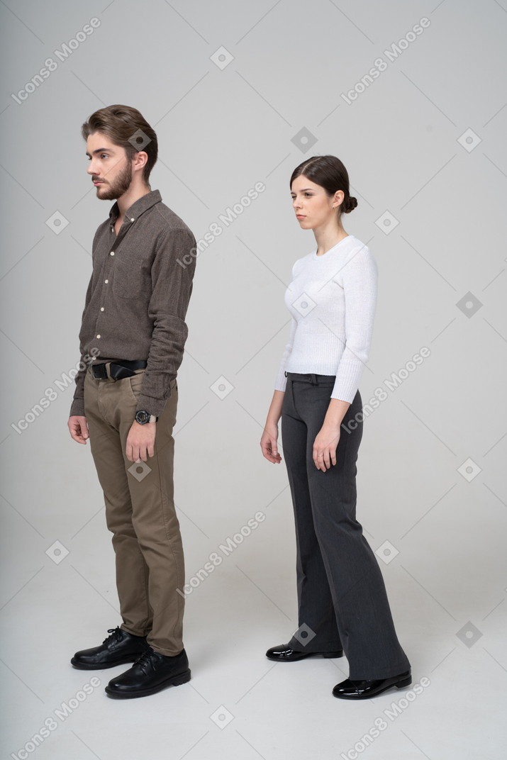 じっと立っているオフィス服でまばたきの若いカップルの4分の3のビュー