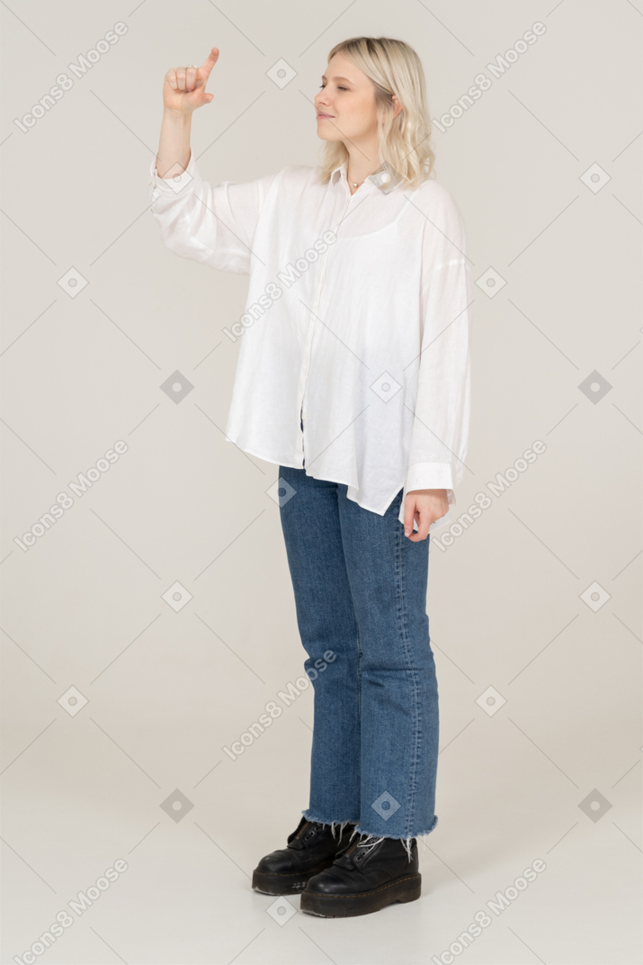 Vista de três quartos de uma mulher loira alegre levantando o dedo e apontando para cima