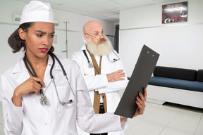 An old doctor standing next to a nurse with clipboard