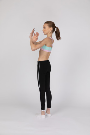 Vista lateral de uma adolescente em roupas esportivas mostrando gesto de parada