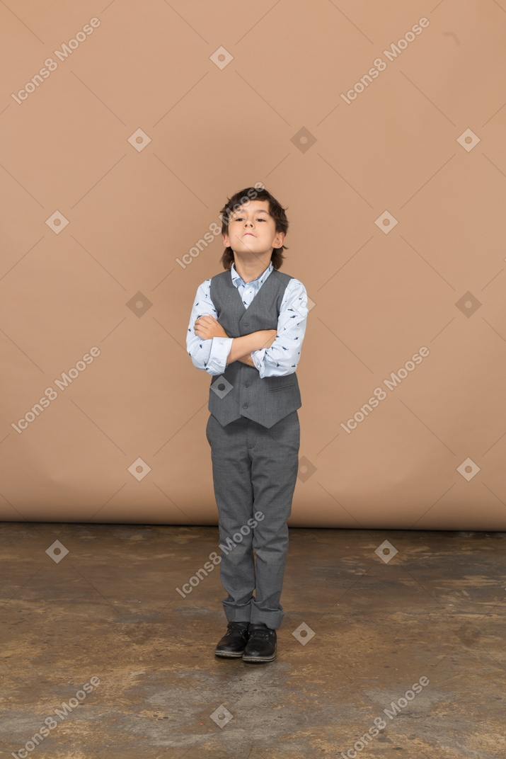 一个穿着灰色西装的男孩交叉双臂站立的正面图