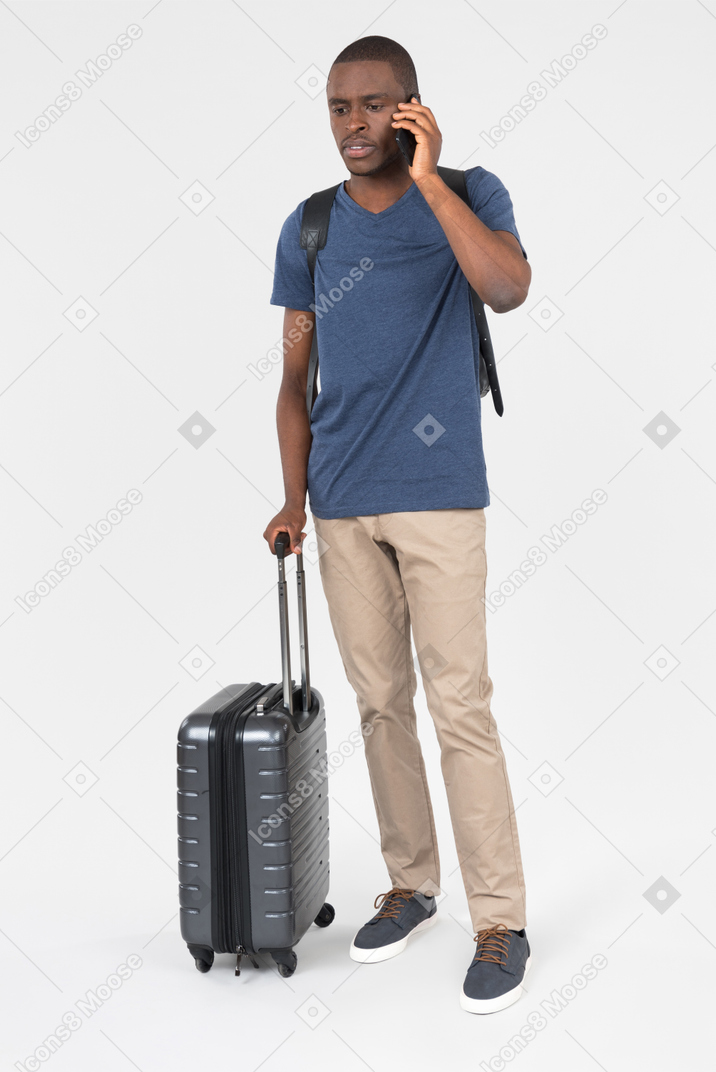 Male black tourist carrying luggage and talking on the phone