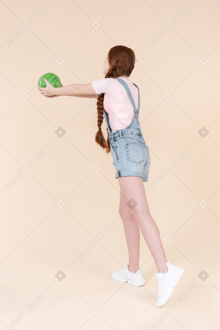 Teenage girl standing half sideways back to camera and holding ball