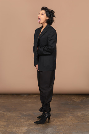 Dreiviertelansicht einer geschäftsfrau in einem schwarzen anzug, die sich nach vorne beugt und zunge zeigt