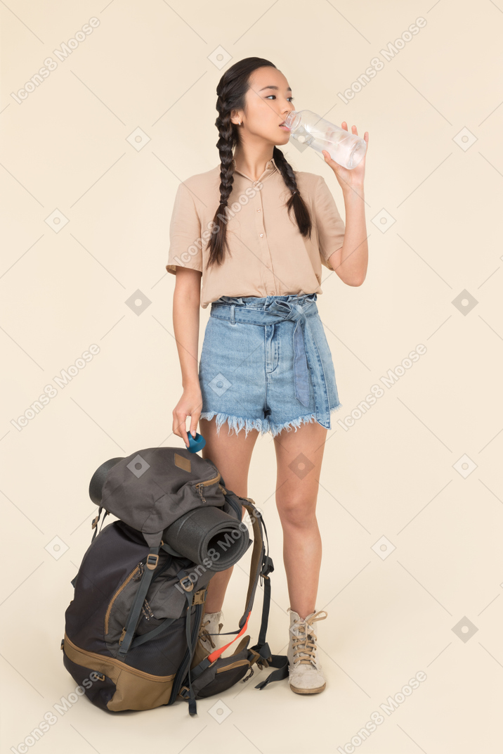 Молодая азиатская женщина, держащая рюкзак и питьевая вода из бутылки
