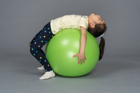 小女孩躺在她背上的绿色健身球上