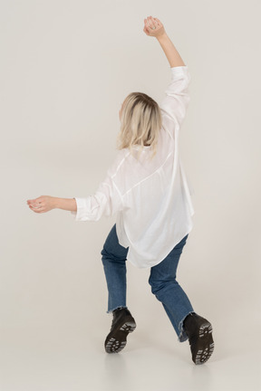 Vista traseira de uma mulher loira em roupas casuais dançando na ponta dos pés e levantando as mãos