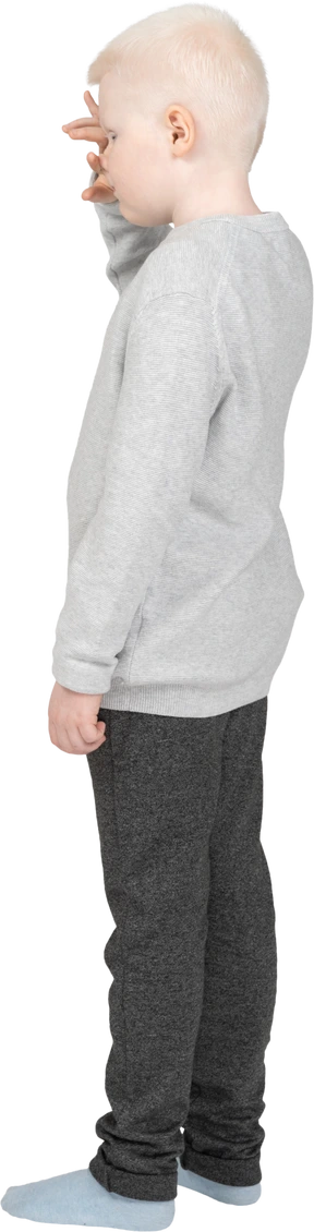 Back three-quarter view of a lonely kid boy in casual clothes touching forehead
