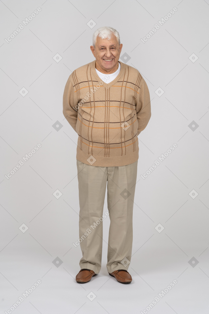 Front view of a happy old man in casual clothes standing with hands behing back