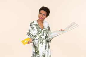 Black short-haired woman in a white and green dress, standing with an international passport and a map in her hands