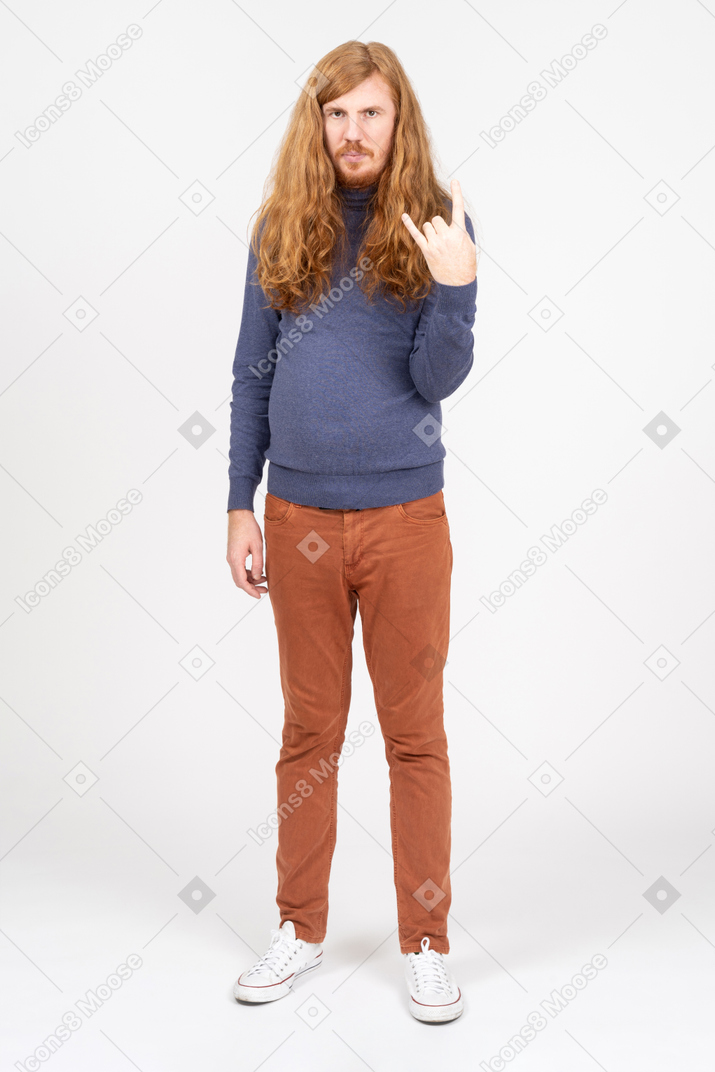 Front view of a young man in casual clothes making rock on gesture and looking at camera