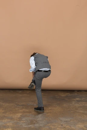Rear view of a boy in suit standing on one leg