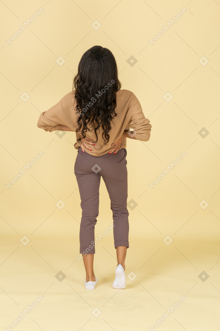 Back view of a dark-skinned young female putting hands on hips & leaning back