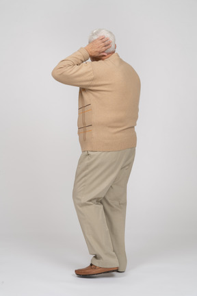 Vista lateral de un anciano con ropa informal posando con la mano en la cabeza