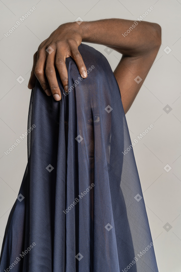 Vista frontal de un joven afro cubierto con un chal azul oscuro tocando su cabeza