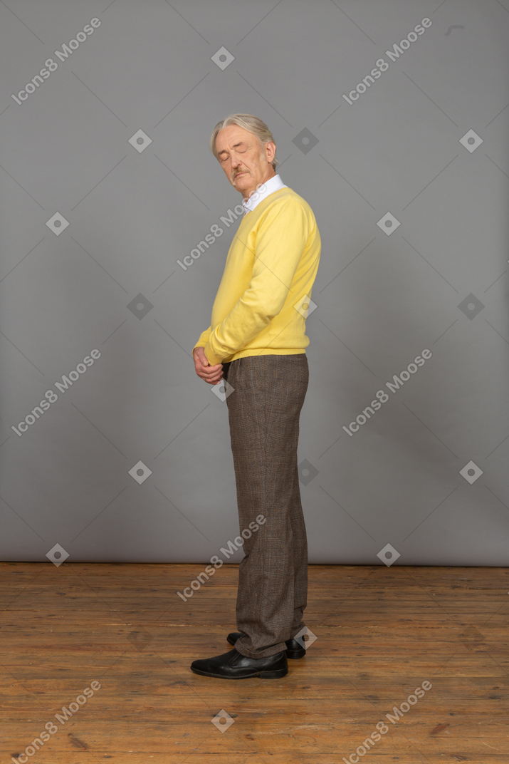 一个老人在黄色套头衫，手牵着手，闭着眼睛的侧视图