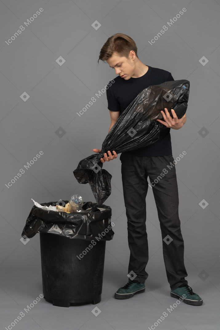 A young man emptying a trash bag into a waste bin
