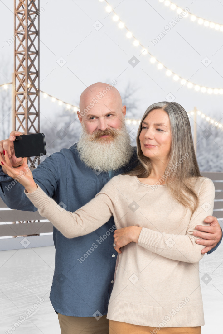 An old couple taking a selfie on an ice rink