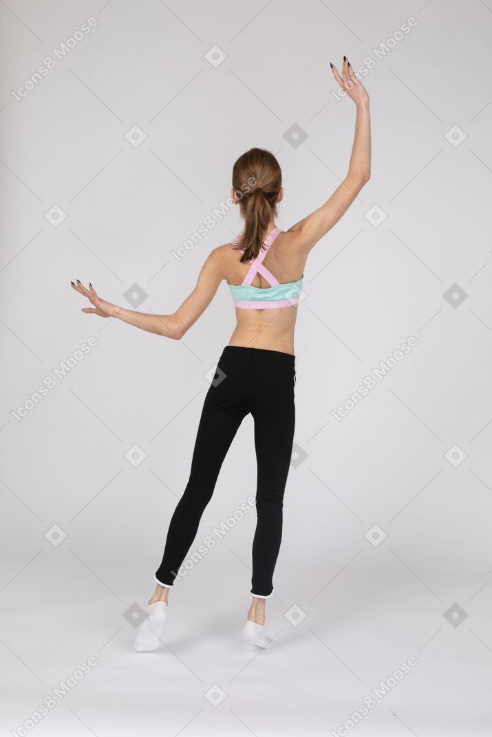 Vista posterior de una jovencita en ropa deportiva levantando las manos y poniendo su pierna a un lado