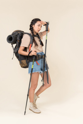 Tired hiker woman walking using trekking poles and drying her forehead with hand