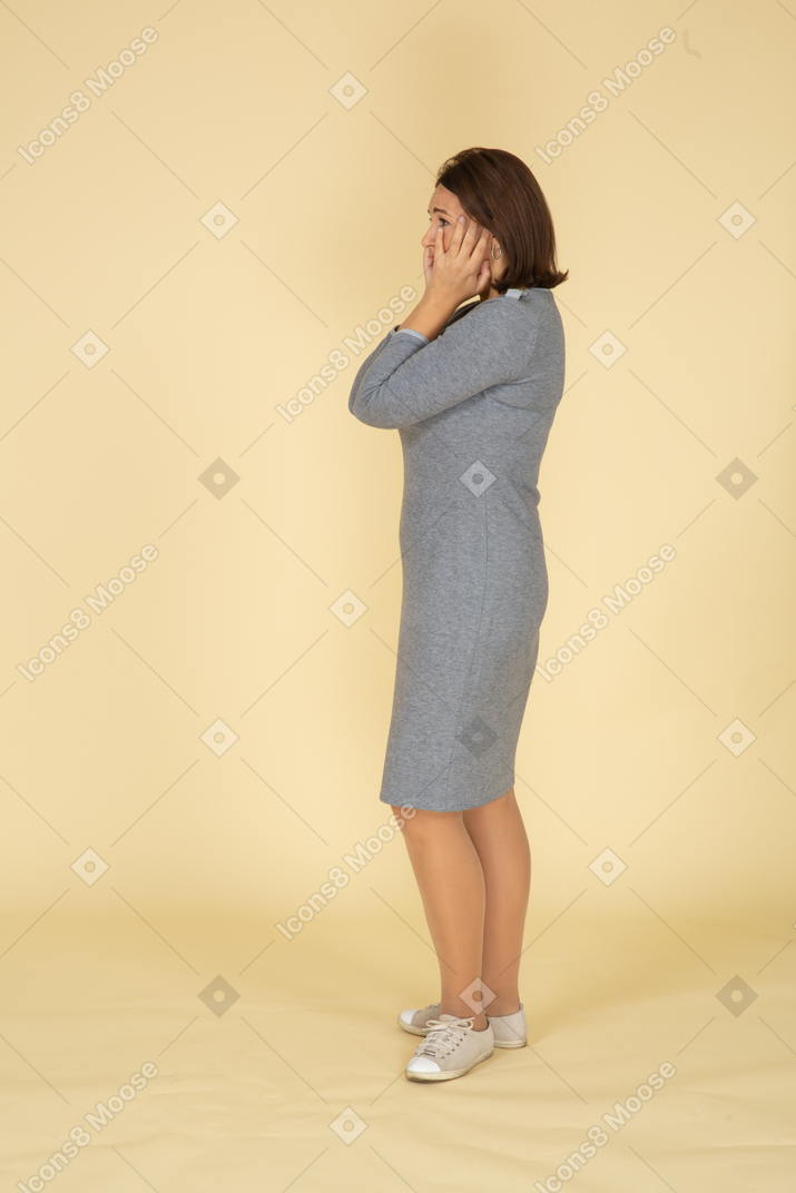 Side view of a sad woman in grey dress touching her face