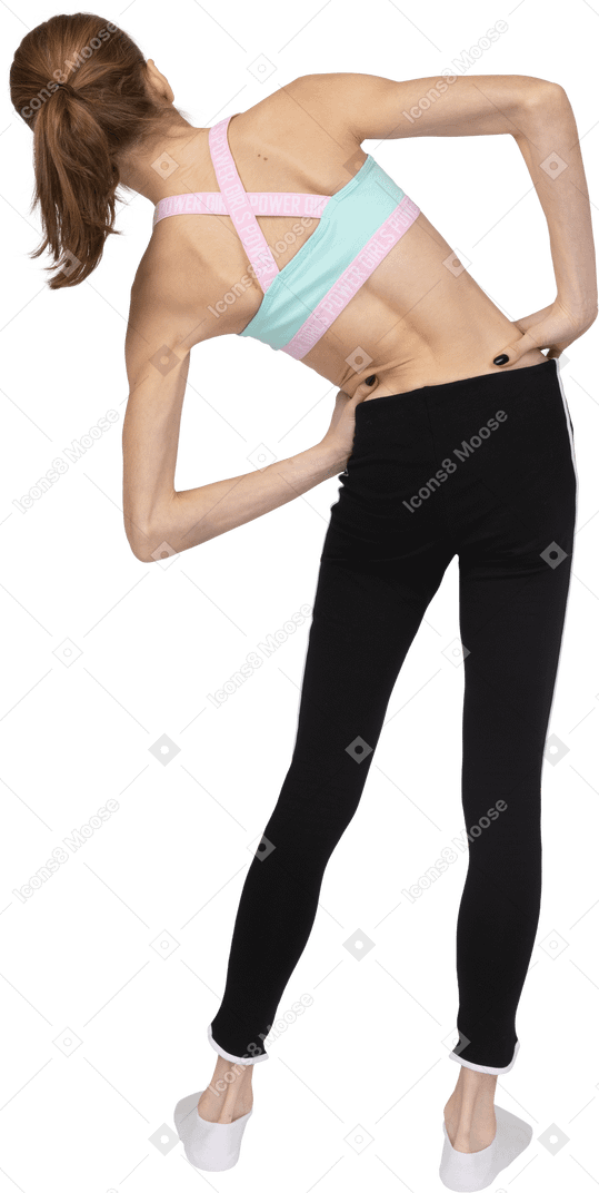 Vista posterior de una jovencita en ropa deportiva poniendo las manos en las caderas mientras se inclina hacia la izquierda