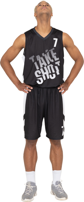 Front view of a young male basketball player putting hands on hips & looking up