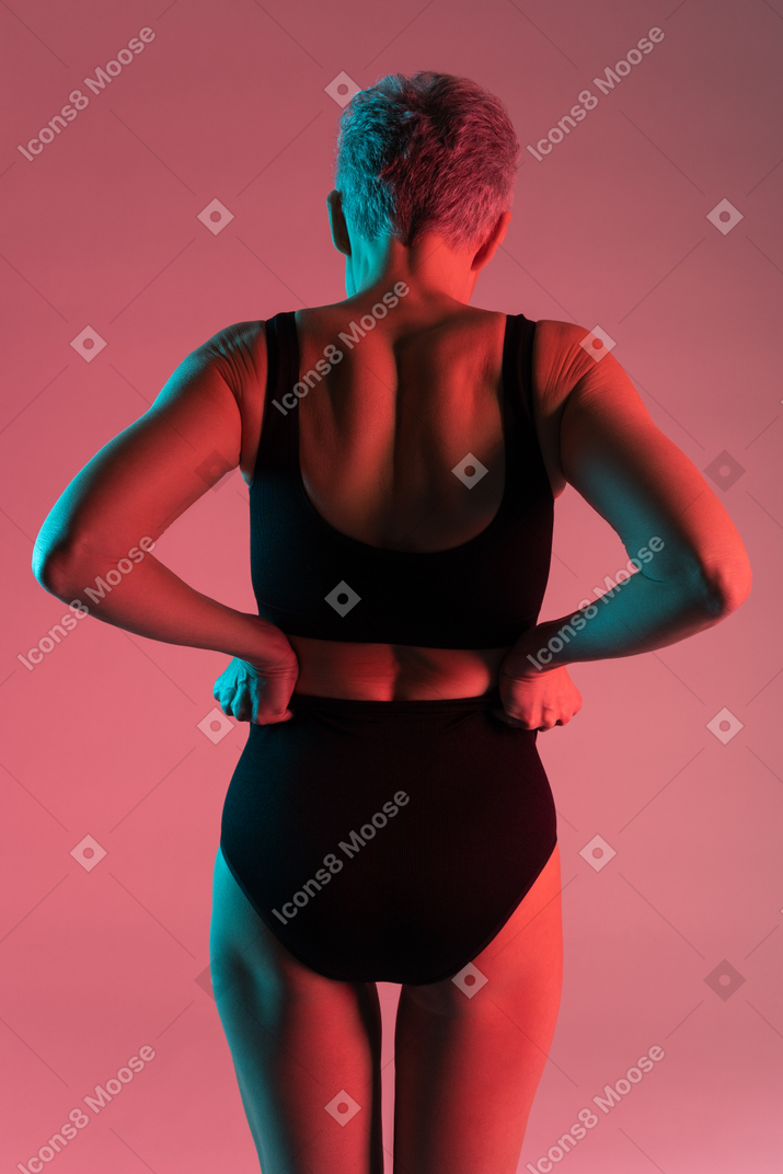 Woman in black lingerie holding arms akimbo back to camera