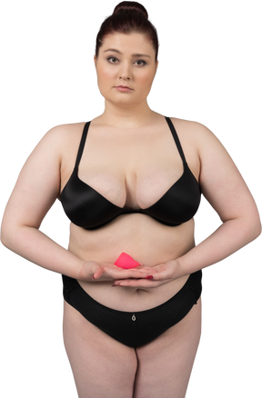 Mulher com corpo positivo em lingerie preta segurando copo menstrual rosa
