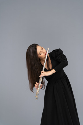 Front view of a serious young lady in black dress playing the flute