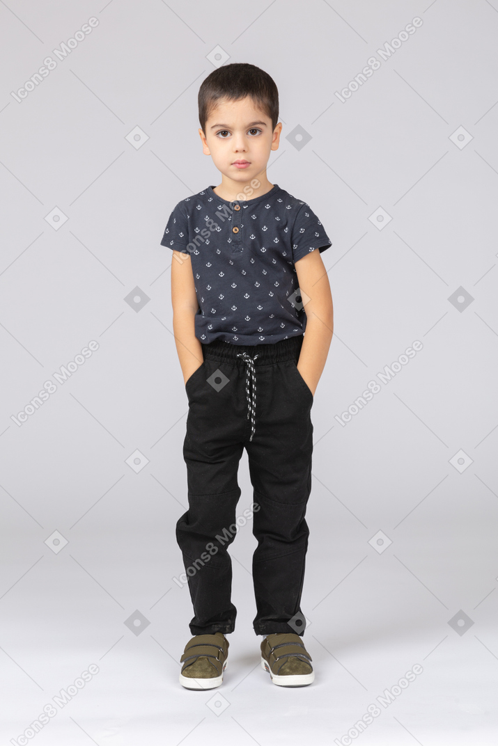 Front view of a cute boy posing with hands in pockets and looking at camera