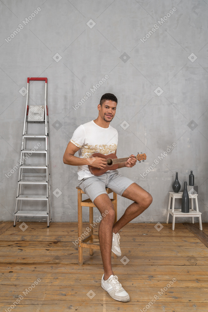 Three-quarter view of a man playing ukulele on a stool