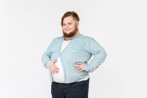 Young overweight man in tight shirt holding hand on belly