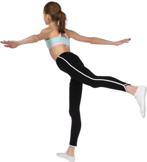 Vista posterior de tres cuartos de una jovencita en ropa deportiva de equilibrio sobre su pierna