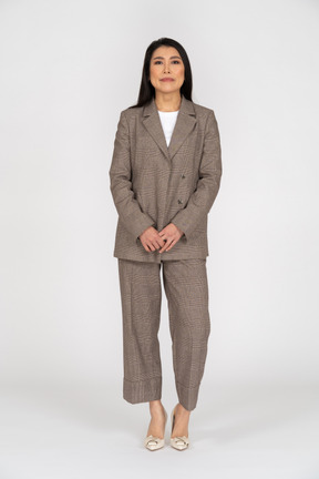 Front view of a confused young lady in brown business suit holding hands together