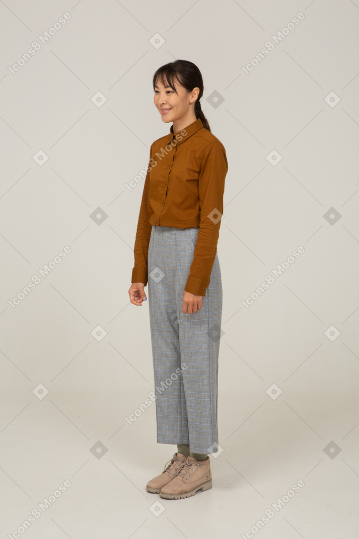 Vista de tres cuartos de una sonriente joven mujer asiática en calzones y blusa inmóvil