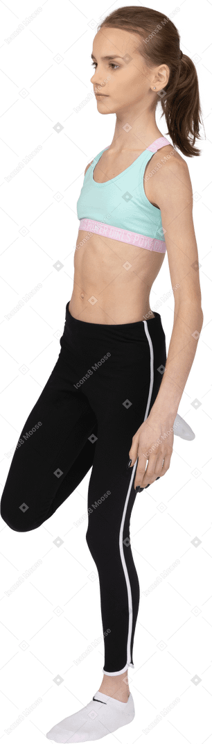 Вид сбоку девушки-подростка в спортивной одежде, поднимающей ногу и держащей лодыжку