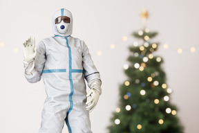 A man in a protective suit standing next to a christmas tree and waving