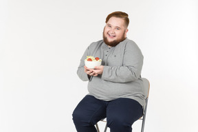 Laughing big bearded man sitting and holding salad