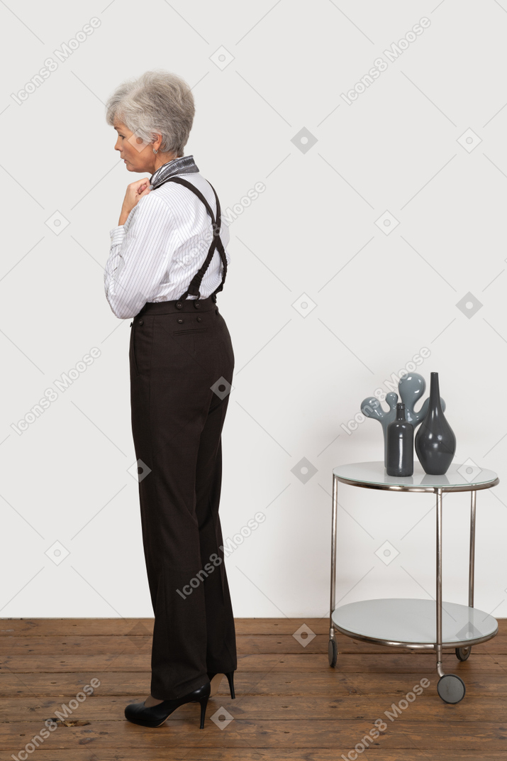 Вид сбоку взволнованной старушки в офисной одежде, касающейся ее воротника