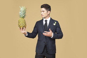 Groom in black suit holding a pineapple and like complimenting it