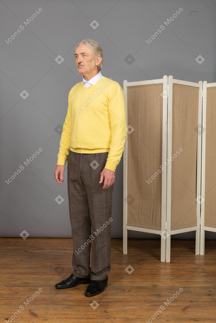 Vista de três quartos de um homem idoso parado e pressionando os lábios