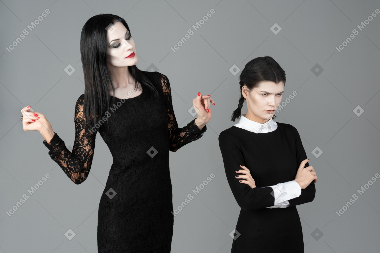 Morticia addams looking at wednesday which is standing with her hands folded