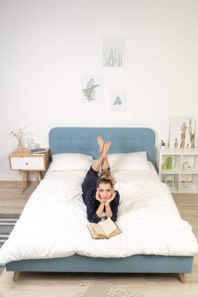 Vorderansicht einer jungen frau, die ein buch im bett liest