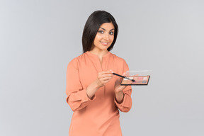 Indian woman holding eyeshadow and eye brush