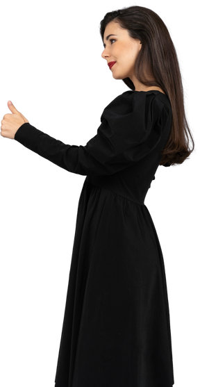 Side view of a smiling young lady in a black dress showing a thumb up