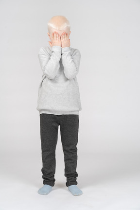 Vista frontal de um menino cobrindo o rosto com as mãos