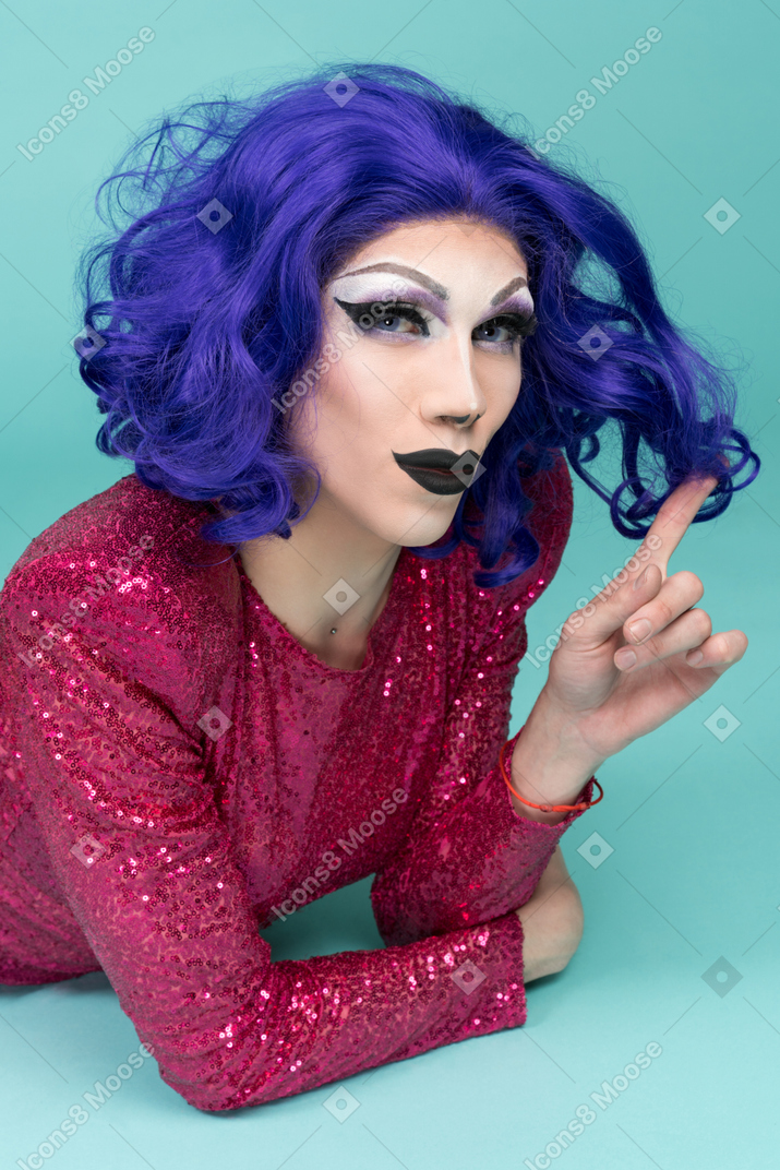Primer plano de una drag queen sonriendo mientras envuelve el rizo alrededor del dedo
