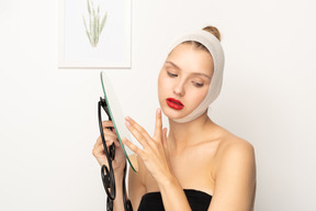 Young woman with bandaged head holding a mirror