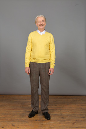 Vue de face d'un vieil homme souriant portant un pull jaune et regardant la caméra
